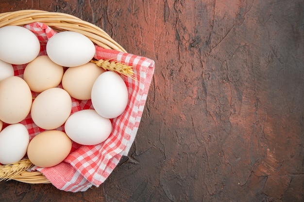 Vue de dessus des œufs de poule blancs à l'intérieur du panier avec une serviette sur la table sombre