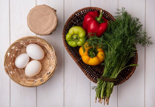 Vue de dessus des œufs de poule dans un panier avec du yaourt dans un pot avec de l'aneth et des poivrons sur fond blanc