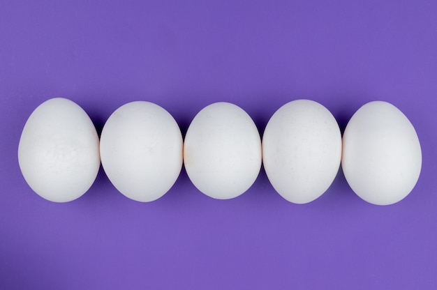 Vue de dessus des œufs de poule frais et sains blancs disposés en ligne sur fond violet