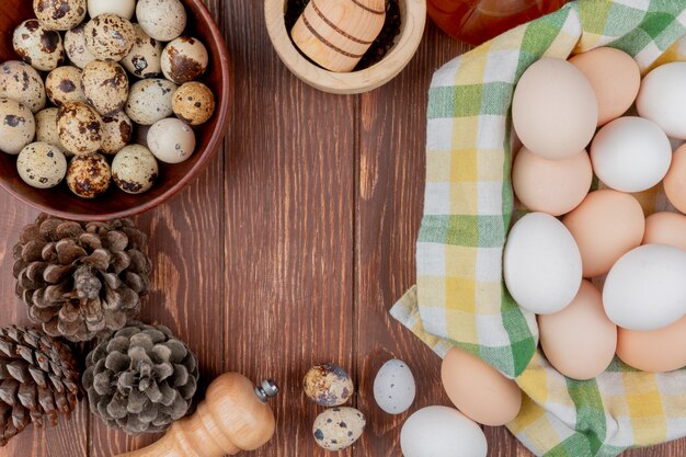 Vue de dessus des œufs de poule sur une nappe vérifiée et des œufs de caille sur un bol avec des pommes de pin isolé sur un fond en bois