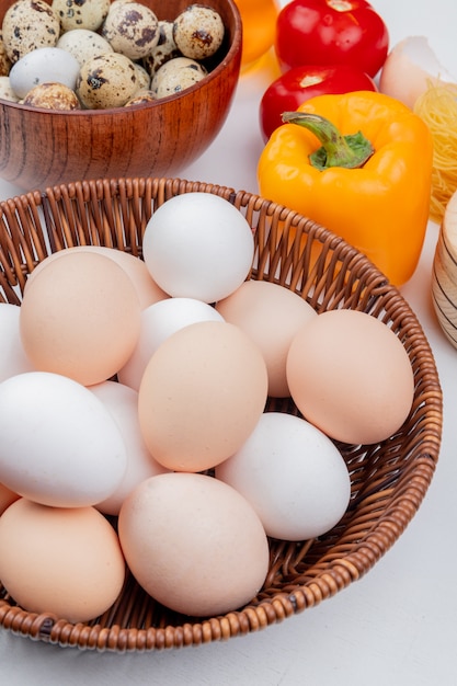 Photo gratuite vue de dessus des œufs de poule sur un seau avec des œufs de caille sur un bol en bois avec des légumes sur fond blanc