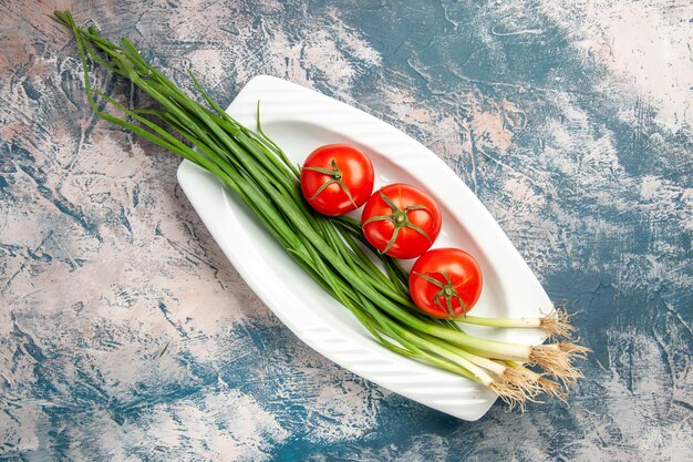 Vue de dessus oignon vert frais avec tomates sur fond bleu clair