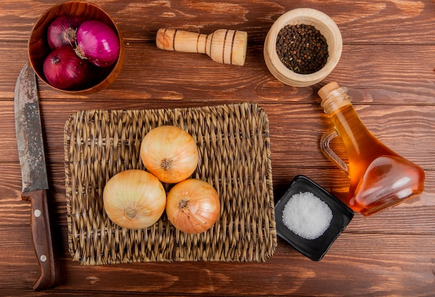 Vue de dessus des oignons rouges et sucrés dans un bol et dans une assiette avec du beurre, du sel, des graines de poivre noir et un couteau sur fond de bois