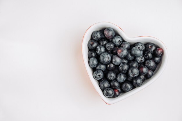 Vue de dessus des olives noires dans un bol en forme de coeur sur fond blanc. espace horizontal pour le texte