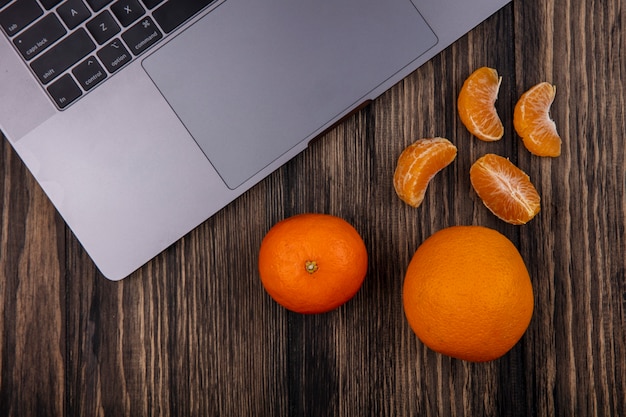Photo gratuite vue de dessus des oranges avec des coins pelés et un ordinateur portable sur un fond en bois