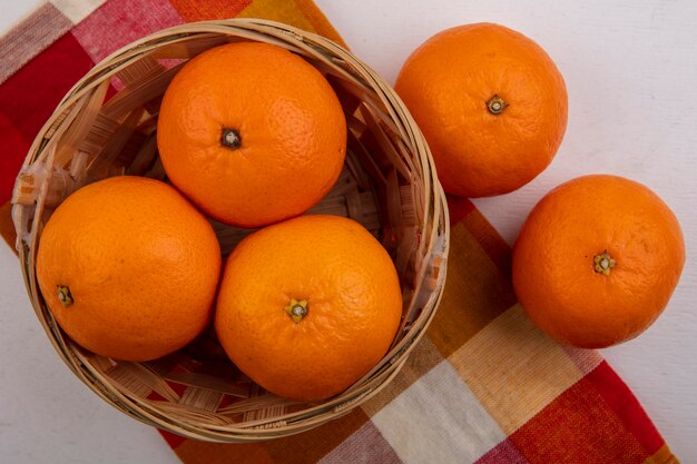 Vue de dessus des oranges dans un panier sur une serviette à carreaux sur fond blanc