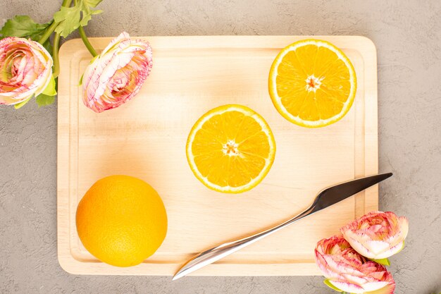 Une vue de dessus des oranges fraîches aigre mûres tranchées et des agrumes tropicaux moelleux avec des roses séchées vitamine jaune sur le bureau de la crème