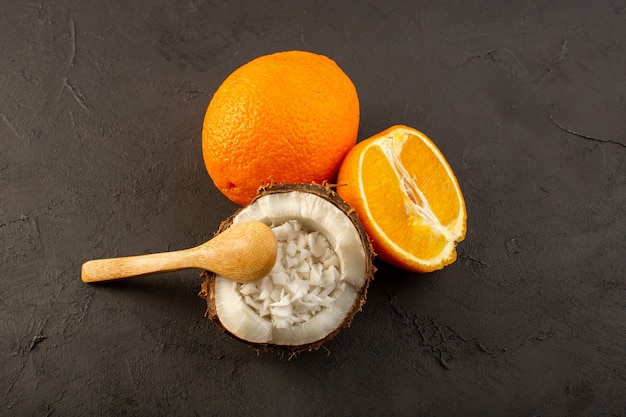 Une vue de dessus des oranges fraîches fruits juteux moelleux avec des tranches de noix de coco sur le jus de fruits exotiques fond sombre