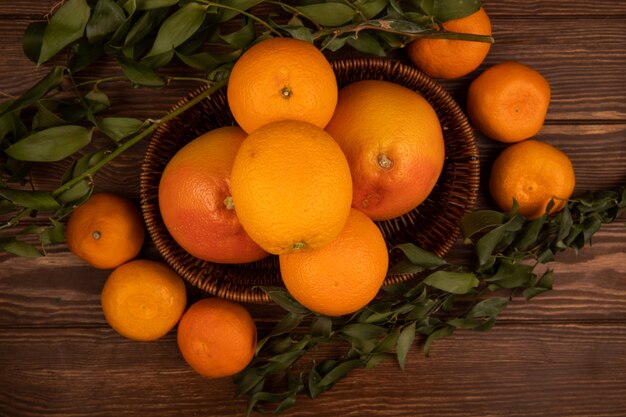 Vue de dessus d'oranges mûres fraîches dans un panier en osier et feuilles vertes sur bois foncé