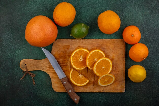 Vue de dessus les oranges sur une planche à découper avec couteau citron lime et pamplemousse sur fond vert