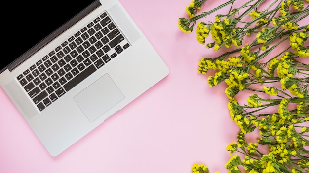 Une vue de dessus d&#39;un ordinateur portable et des fleurs jaunes sur fond rose