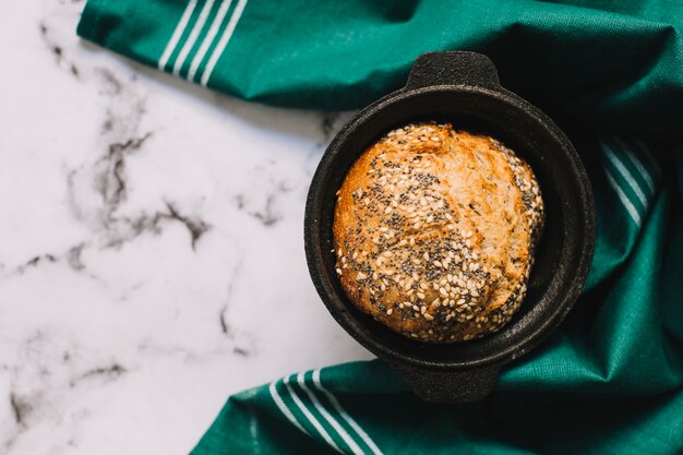 Une vue de dessus de pain fraîchement cuit au four dans un ustensile avec une serviette verte sur fond de marbre