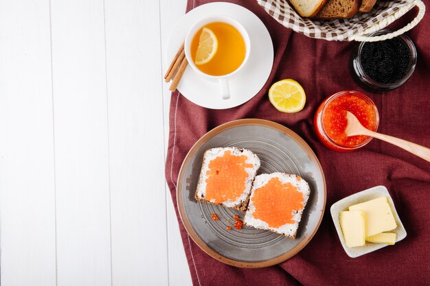 Vue de dessus pain de seigle grillé au caviar rouge avec du fromage cottage beurre de caviar rouge caviar noir pain blanc tasse de thé cannelle tranche de citron et copie espace sur fond blanc