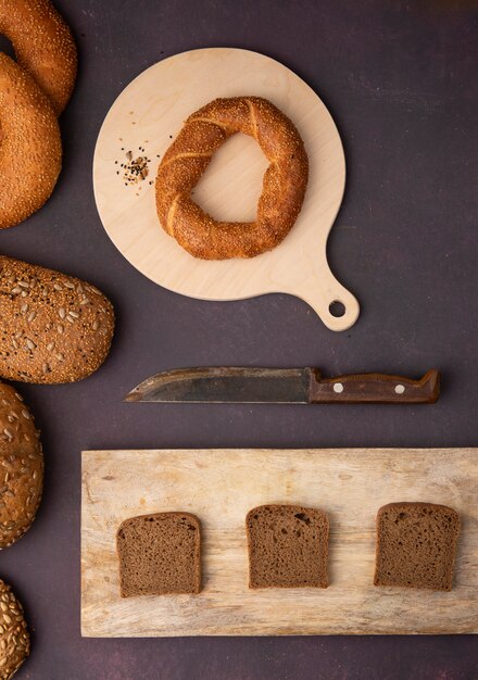 Vue de dessus des pains comme bagel et pain de seigle en tranches sur des planches à découper avec un couteau sur fond marron