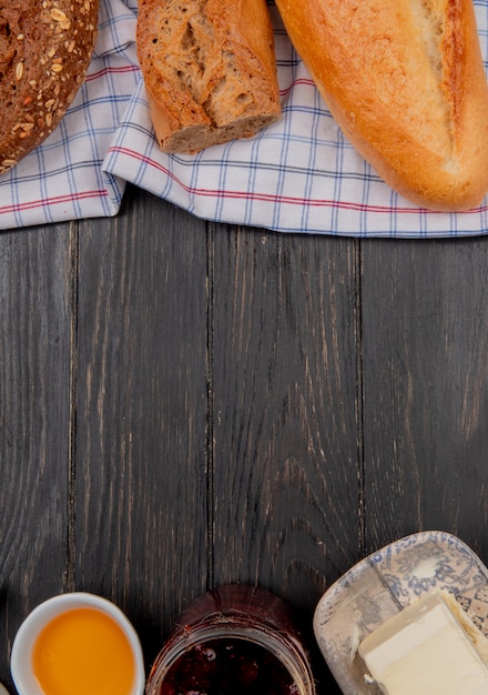 Vue de dessus des pains comme des baguettes noires vietnamiennes ensemencées sur un tissu avec des beurres et de la confiture sur une table en bois avec copie espace