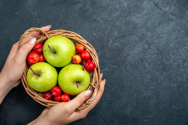 Vue de dessus panier avec fruits pommes et cerises douces sur arbre de fraîcheur de composition de baies de fruits de surface gris foncé