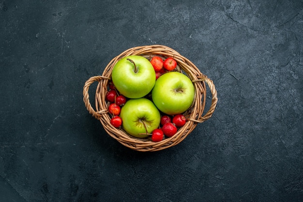 Vue de dessus panier avec fruits pommes et cerises douces sur arbre de fraîcheur de composition de baies de fruits de surface sombre