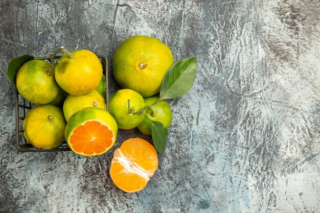 Vue de dessus d'un panier avec des mandarines vertes fraîches coupées en deux et des mandarines pelées sur le côté droit du fond gris