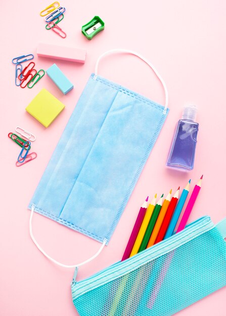 Vue de dessus de la papeterie de retour à l'école avec des crayons colorés et un masque médical
