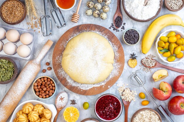 Vue de dessus de la pâte crue sur une râpe ronde en bois et un ensemble d'aliments sur fond de glace