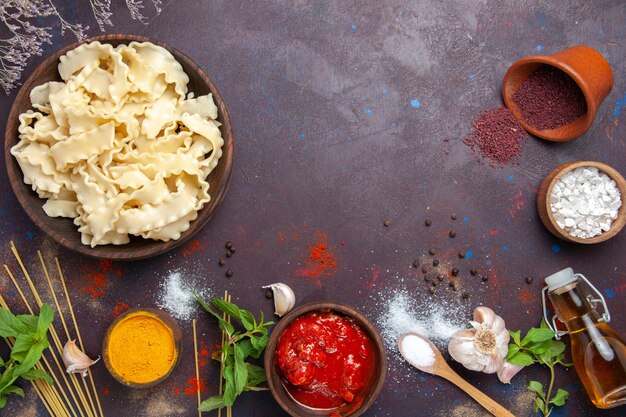 Vue de dessus de la pâte crue en tranches avec des assaisonnements sur fond sombre pâte pâtes repas dîner alimentaire