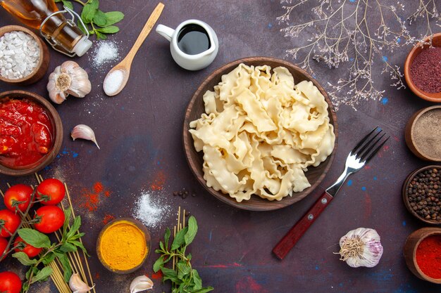 Vue de dessus de la pâte crue en tranches avec des assaisonnements sur la pâte de pâtes repas dîner fond sombre