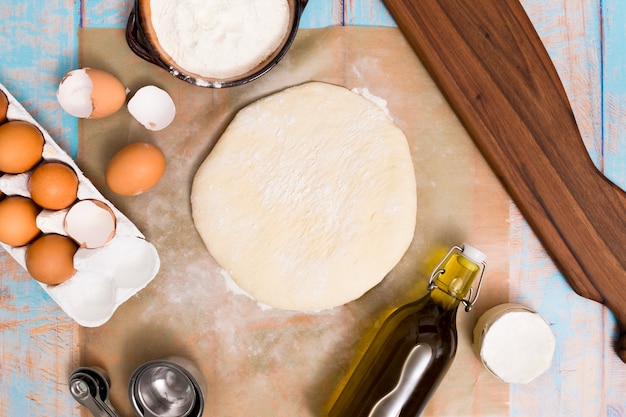 Une vue de dessus de la pâte plate; farine; des œufs; cuillère à mesurer et huile sur table en bois