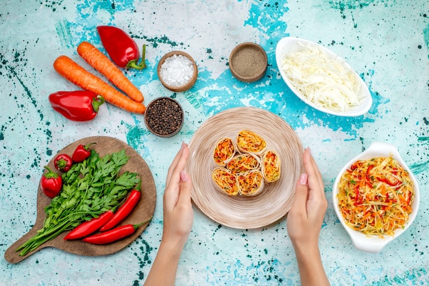 Vue de dessus de la pâte de rouleaux de légumes en tranches avec une garniture savoureuse avec salade de carottes vertes et poivrons rouges épicés sur le bureau bleu vif