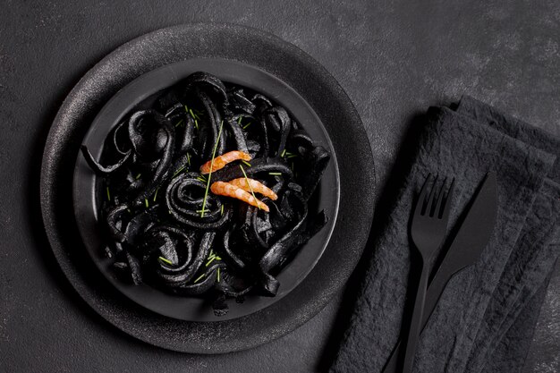 Vue de dessus des pâtes aux crevettes noires et des couverts noirs