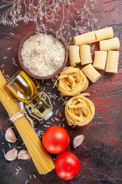 Vue de dessus des pâtes crues avec du riz et des tomates sur la surface sombre de la pâte de pâtes crues