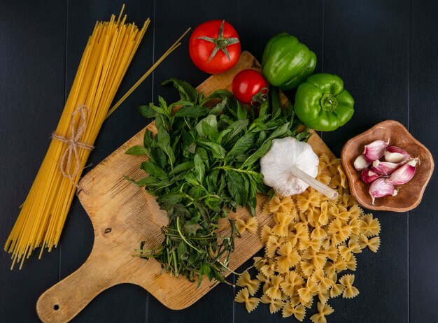 Vue de dessus des pâtes crues avec spaghetti tomates ail et poivron à la menthe sur une planche à découper sur une surface noire