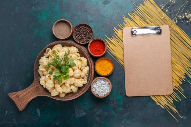 Vue de dessus des pâtes cuites avec bloc-notes et différents assaisonnements sur une surface sombre