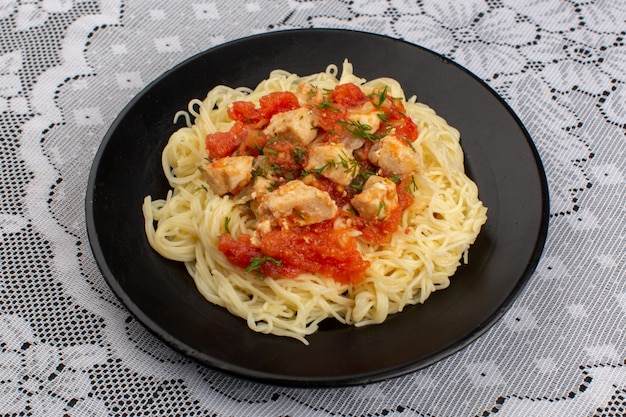 Vue de dessus des pâtes cuites savoureuses avec des ailes de poulet cuites et de la sauce tomate à l'intérieur de la plaque noire sur la table