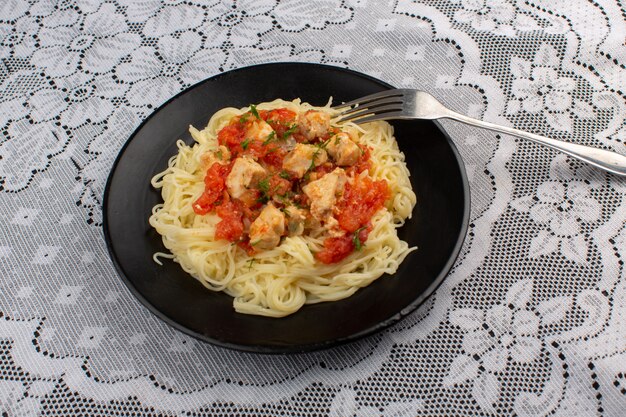 Vue de dessus des pâtes cuites savoureuses avec des tranches de poulet et de la sauce tomate à l'intérieur de la plaque noire sur la table