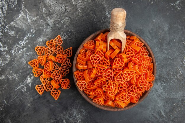 Vue de dessus pâtes italiennes coeurs rouges cuillère en bois dans un bol sur une table sombre avec espace de copie