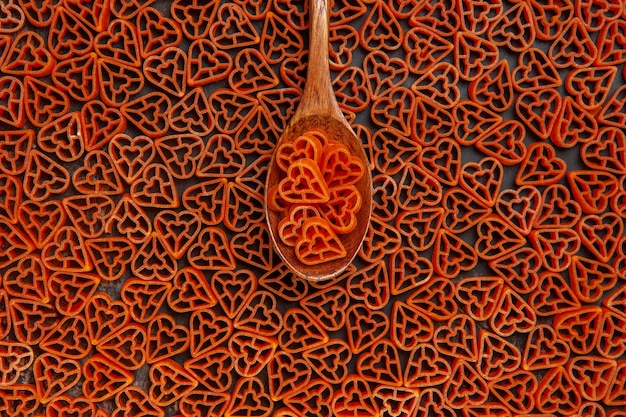 Photo gratuite vue de dessus des pâtes italiennes coeurs rouges sur cuillère et sur table sombre