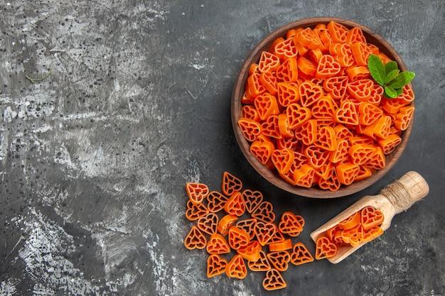 Photo gratuite vue de dessus des pâtes italiennes coeurs rouges dans un bol cuillère en bois sur un lieu de copie de table sombre