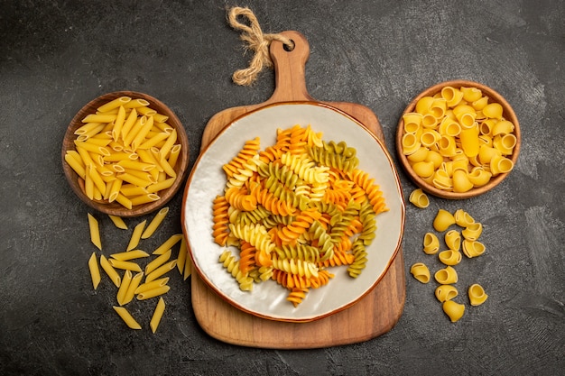 Vue de dessus des pâtes italiennes crues à l'intérieur des assiettes brunes sur gris foncé