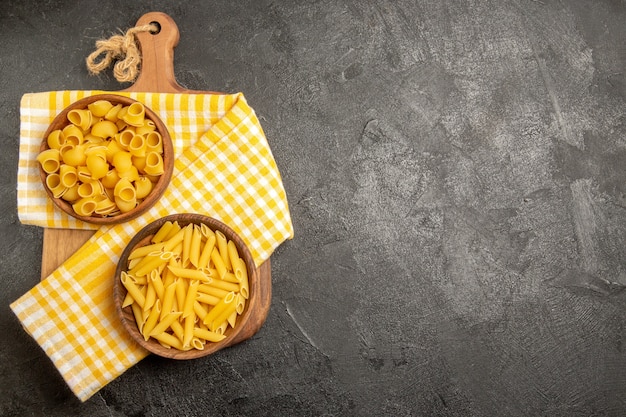 Vue de dessus des pâtes italiennes crues à l'intérieur des assiettes brunes sur le gris