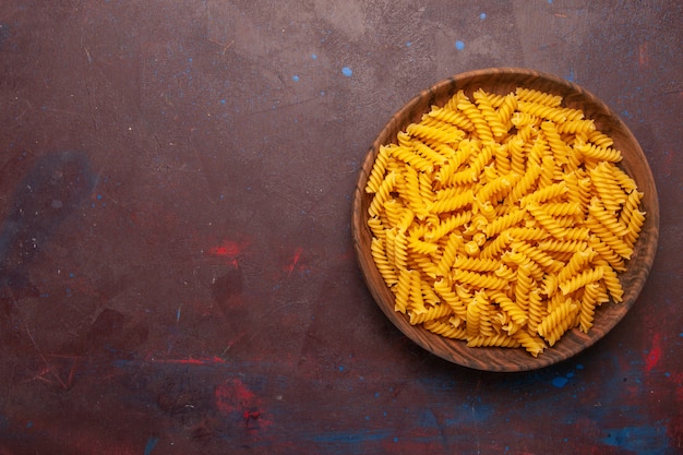 Vue de dessus des pâtes italiennes crues à l'intérieur du plateau en bois sur un bureau sombre produit repas alimentaire légume