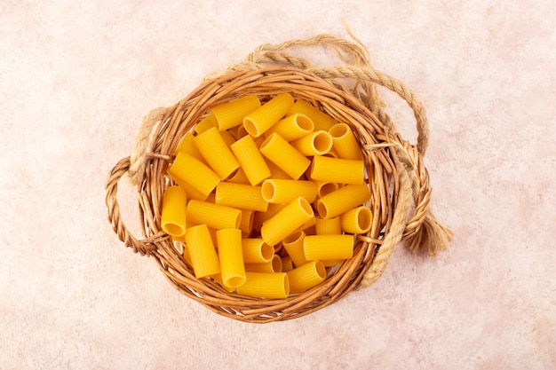 Une vue de dessus des pâtes italiennes crues jaune à l'intérieur du petit panier avec des cordes sur rose