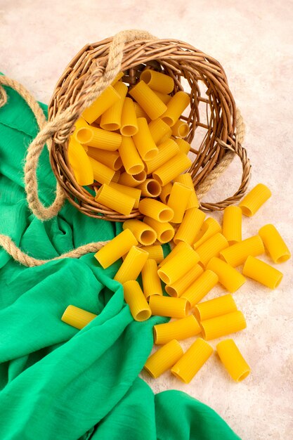 Une vue de dessus pâtes italiennes crues jaune à l'intérieur du petit panier avec des cordes sur tissu vert et rose