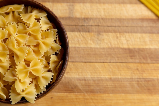 Photo gratuite une vue de dessus des pâtes italiennes crues peu formé à l'intérieur de la plaque brune sur le bureau en bois de pâtes italiennes repas