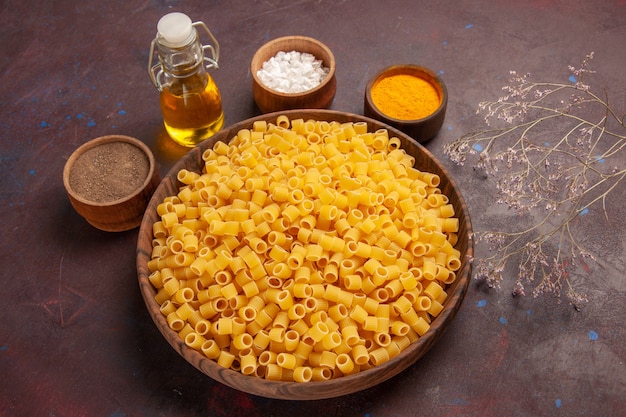 Vue de dessus pâtes italiennes crues peu formé à l'intérieur de la plaque sur un bureau sombre pâtes alimentaires dîner de pâte crue beaucoup