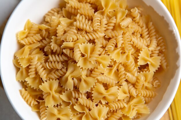 Une vue de dessus des pâtes italiennes crues peu formées sur le bureau en bois de pâtes italiennes repas