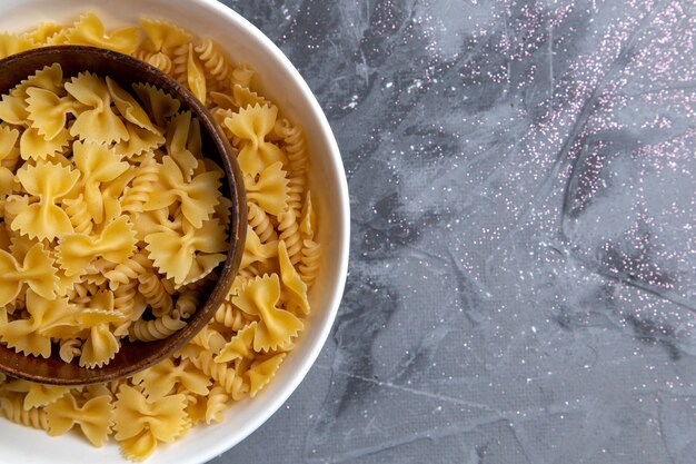 Une vue de dessus des pâtes italiennes crues peu et longtemps formées à l'intérieur de la plaque brune et blanche sur le bureau gris pâtes alimentaires repas italien