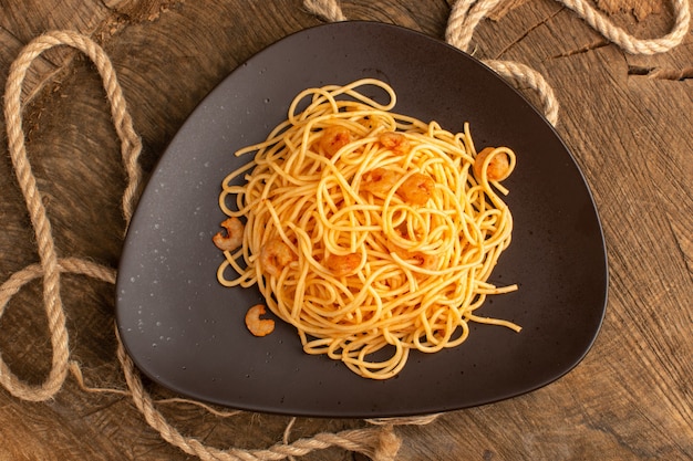 Vue de dessus des pâtes italiennes cuites aux crevettes à l'intérieur de la plaque brune avec des cordes sur le bureau en bois