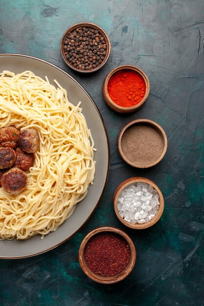 Vue de dessus des pâtes italiennes cuites avec des boulettes de viande et des assaisonnements sur la surface bleu foncé