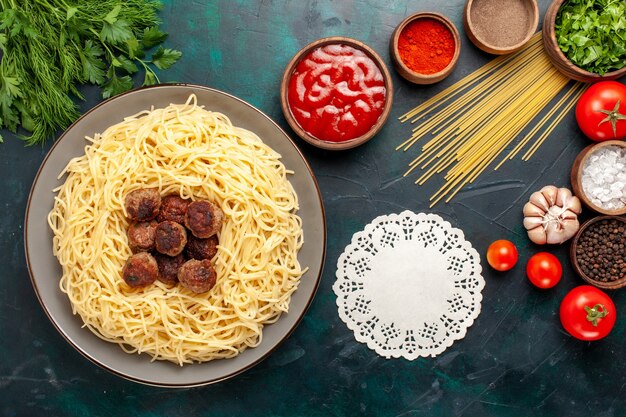 Vue de dessus des pâtes italiennes cuites avec des boulettes de viande et différents assaisonnements sur la surface bleu foncé