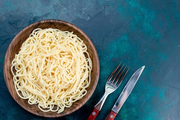 Vue de dessus des pâtes italiennes cuites à l'intérieur d'une plaque en bois ronde sur un bureau bleu foncé pâtes italie nourriture dîner pâte viande